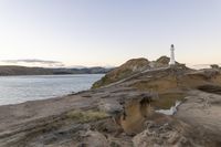 a large white lighthouse is standing on the rocks by the water's edge as a bright light shines brightly in the sky