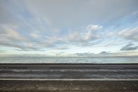 view of the ocean with a sky full of clouds, and a bench sitting along side it