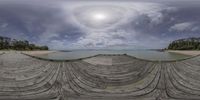 a fish eye lens picture shows the view of water, beach and a dock at a pier