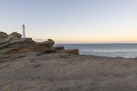 a lighthouse on the edge of a cliff overlooking the ocean and rocks in front of the light house