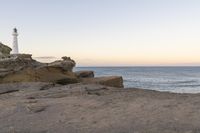 a lighthouse on the edge of a cliff overlooking the ocean and rocks in front of the light house