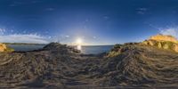 panorama of the ocean, sand and sky from a panorama fisheye lens, showing a view of the sun and sand piles