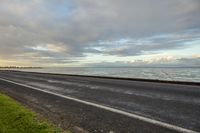 empty road on the edge of a wide body of water at dusk with cloudy skies above