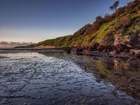 a beach with a rock formation in the foreground and water on the sand below