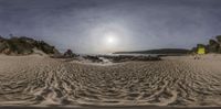 some sand water water and sand rocks and trees with the sun in the distance and sky