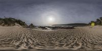 some sand water water and sand rocks and trees with the sun in the distance and sky