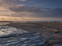 a very small boat sitting in the water on a beach at sunset with rocks and seaweed