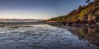 a couple stands on the sand while the sun is setting over the sea and hill