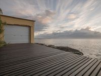 a wooden deck next to a beach and a building with doors open on a cloudy day