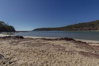 a deserted sandy beach next to the water and hills on a clear day, in the sunshine