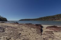 a deserted sandy beach next to the water and hills on a clear day, in the sunshine