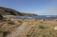 an open dirt path runs to the water near a grassy area near rocks and vegetation