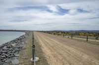 a dirt road stretches out toward the water and a lake with large rocks in the middle of it