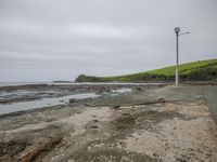 an empty concrete platform at the edge of the ocean with the grass on it, and water surrounding