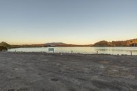 an empty parking lot sitting next to the water with mountains in the distance behind it