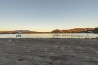 an empty parking lot sitting next to the water with mountains in the distance behind it
