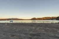 an empty parking lot sitting next to the water with mountains in the distance behind it