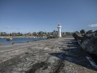 an empty pier by the water and lighthouse surrounded by rocks and houses with many boats