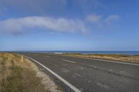 an empty road leading into the ocean in a field near a beach with grass and rocks