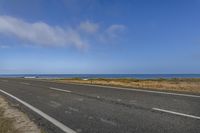 an empty road leading into the ocean in a field near a beach with grass and rocks