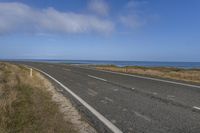 an empty road leading into the ocean in a field near a beach with grass and rocks