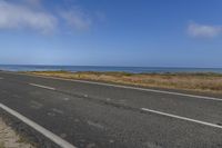 an empty road leading into the ocean in a field near a beach with grass and rocks