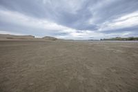 an empty sandy beach, with a lake and mountains in the background and sand on the shore