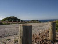 an empty gravel road with poles along it by the water and ocean in the distance