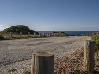 an empty gravel road with poles along it by the water and ocean in the distance