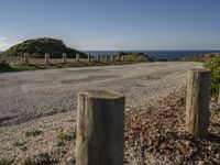 an empty gravel road with poles along it by the water and ocean in the distance