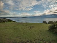 there is a large grassy field near the ocean and sand beach area that overlooks the coastline