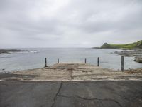 a dock is overhangng the water in front of the ocean with rocks and grass