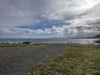 the sea is in the foreground and a grassy bank near the shore and rocks under stormy skies