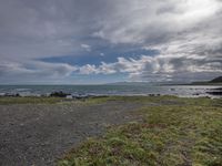 the sea is in the foreground and a grassy bank near the shore and rocks under stormy skies