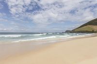 a person riding a surf board on a beach by the ocean with waves and hills