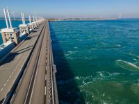 the bridge has two lanes across it that can go along the water or land, in an area with wind turbines