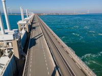 the bridge has two lanes across it that can go along the water or land, in an area with wind turbines