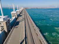 the bridge has two lanes across it that can go along the water or land, in an area with wind turbines