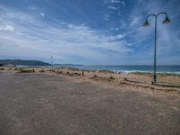 an empty road with a beach and ocean in the background and fence surrounding it with barbed posts