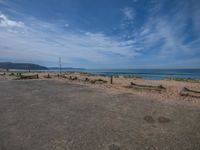 an empty road with a beach and ocean in the background and fence surrounding it with barbed posts