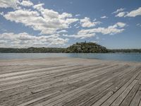 there is a wooden floor by the water on top of it with the beach and hills in the background