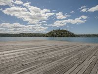 there is a wooden floor by the water on top of it with the beach and hills in the background