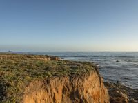 a grassy field by the shore and a cliff with rocks in the ocean in the background