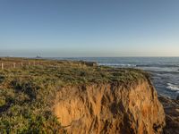 a grassy field by the shore and a cliff with rocks in the ocean in the background