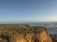 a grassy field by the shore and a cliff with rocks in the ocean in the background