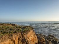 a grassy field by the shore and a cliff with rocks in the ocean in the background