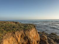 a grassy field by the shore and a cliff with rocks in the ocean in the background