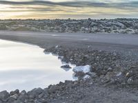 a person walking along the shore near a body of water at sunset and a bench