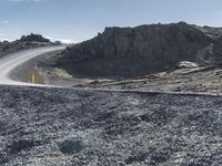 a curved dirt road leads down a mountain with a road sign in the foreground