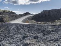 a curved dirt road leads down a mountain with a road sign in the foreground